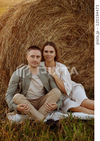 A couple is sitting on the grass next to a hay bale A couple is sitting on the grass next to a hay bale 120194473