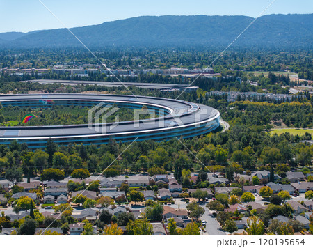 The image captures an aerial view of Apple Park's circular architecture in Cupertino, California, surrounded by greenery, residential areas, and rolling hills. The image captures an aerial view of Apple Park's circular architecture in Cupertino, California, surrounded by greenery, residential areas, and rolling hills. 120195654