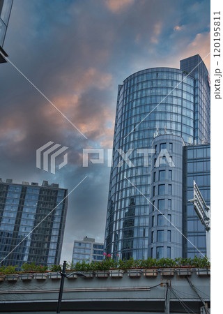 The image captures a modern Shanghai skyline with a cylindrical glass skyscraper reflecting the evening sky, surrounded by high rises and a rooftop garden. 120195811