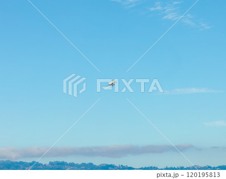 A small airplane flies high in a clear blue sky above faint hilly outlines, likely near San Francisco, with minimal clouds and a vast sky expanse. A small airplane flies high in a clear blue sky above faint hilly outlines, likely near San Francisco, with minimal clouds and a vast sky expanse. 120195813