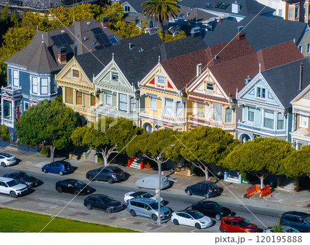 The iconic Painted Ladies in San Francisco are set against lush trees and a clear blue sky, with cars parked along the street in front. The iconic Painted Ladies in San Francisco are set against lush trees and a clear blue sky, with cars parked along the street in front. 120195888