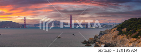 The Golden Gate Bridge's red orange hue contrasts with the bay and Marin County hills. Rugged coastal cliffs and rocks feature in the foreground under a partly cloudy sky. The Golden Gate Bridge's red orange hue contrasts with the bay and Marin County hills. Rugged coastal cliffs and rocks feature in the foreground under a partly cloudy sky. 120195924