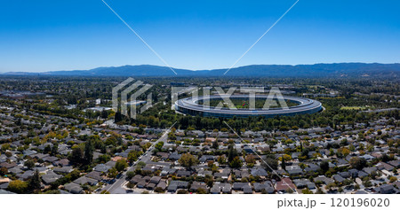 Aerial view of Apple Park in Cupertino, California, with its circular design, surrounded by greenery, residential neighborhoods, and distant mountains. Aerial view of Apple Park in Cupertino, California, with its circular design, surrounded by greenery, residential neighborhoods, and distant mountains. 120196020
