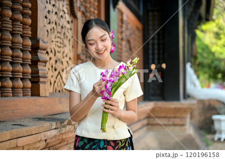 A charming Asian woman stands by the temple, adjusting flowers in her hand. 120196158