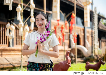 An Asian woman in a traditional Northern Thai dress stands outdoors with a temple in the background An Asian woman in a traditional Northern Thai dress stands outdoors with a temple in the background 120196167