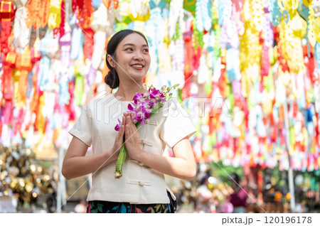 A smiling Asian woman stands in a temple with colorful lanterns in the background. 120196178