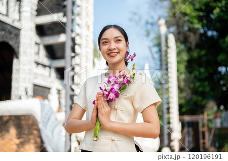 Charming Asian woman in a traditional Thai Lanna dress stands in front of a beautiful ancient temple 120196191