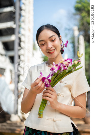 A charming Asian woman in a traditional Lanna dress admires the beautiful orchid bouquet in her hand A charming Asian woman in a traditional Lanna dress admires the beautiful orchid bouquet in her hand 120196192