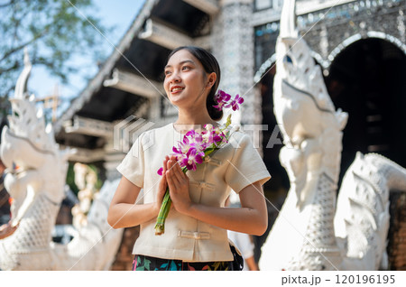 Charming Asian woman in a traditional Thai Lanna dress stands in front of a beautiful ancient temple 120196195
