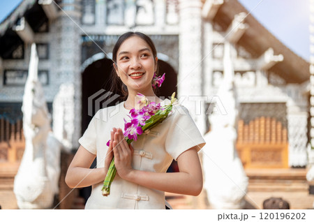 Charming Asian woman in a traditional Thai Lanna dress stands in front of a beautiful ancient temple 120196202