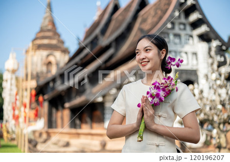 Charming Asian woman in a traditional dress stands outdoors with an ancient temple in the background 120196207