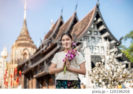 A smiling Asian woman in a traditional dress with a beautiful temple and pagoda in the background. A smiling Asian woman in a traditional dress with a beautiful temple and pagoda in the background. 120196208