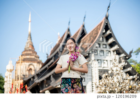 A smiling Asian woman in a traditional dress with a beautiful temple and pagoda in the background. A smiling Asian woman in a traditional dress with a beautiful temple and pagoda in the background. 120196209