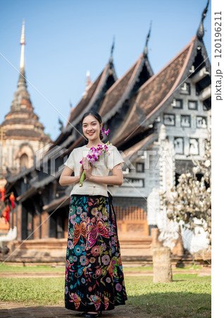 A smiling Asian woman in a traditional dress with a beautiful temple and pagoda in the background. A smiling Asian woman in a traditional dress with a beautiful temple and pagoda in the background. 120196211