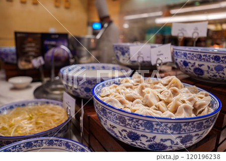 A vibrant display of traditional Chinese dumplings in a blue and white porcelain bowl, set in a bustling Shanghai market with steaming dishes nearby. 120196238