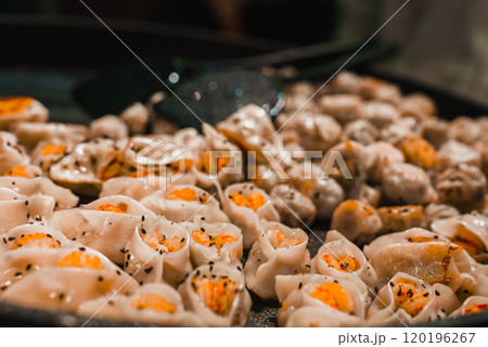 A close up view of dumplings on a pan in Shanghai, featuring translucent wrappers with orange filling and black sesame seeds, highlighting traditional cuisine. A close up view of dumplings on a pan in Shanghai, featuring translucent wrappers with orange filling and black sesame seeds, highlighting traditional cuisine. 120196267