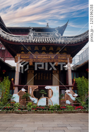 A traditional Chinese building in Shanghai features intricate wooden carvings and a curved roof with dragon motifs, surrounded by greenery and flowers. A traditional Chinese building in Shanghai features intricate wooden carvings and a curved roof with dragon motifs, surrounded by greenery and flowers. 120196288