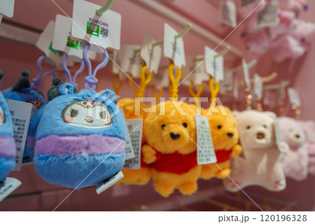 A variety of plush keychains featuring cartoon characters are displayed in a Shanghai store. Blue and purple plushies and yellow bears in red shirts are prominent. A variety of plush keychains featuring cartoon characters are displayed in a Shanghai store. Blue and purple plushies and yellow bears in red shirts are prominent. 120196328
