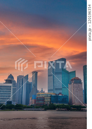 View of Shanghai's Pudong district skyline with the Oriental Pearl Tower, set against a vibrant sunset sky. The Huangpu River flows in the foreground. 120196354