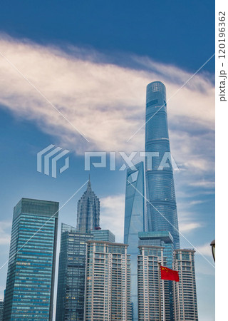 The skyline of Shanghai features the Shanghai Tower, World Financial Center, and Jin Mao Tower under a clear sky with a Chinese flag in the foreground. 120196362