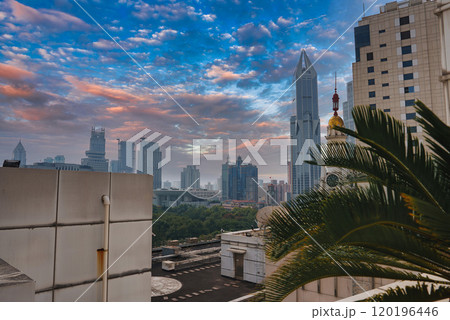 View of Shanghai's skyline featuring the Shanghai World Financial Center, modern skyscrapers, and traditional architecture. Lush greenery and a palm tree in the foreground under a vibrant sunset sky. View of Shanghai's skyline featuring the Shanghai World Financial Center, modern skyscrapers, and traditional architecture. Lush greenery and a palm tree in the foreground under a vibrant sunset sky. 120196446