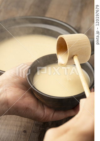 甘酒　温かい甘酒を柄杓で手に持った湯呑みに注ぐ　 120197679