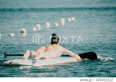 Sea woman sup. Silhouette of happy middle aged tanned woman in rainbow bikini, surfing on SUP board, confident paddling through water surface. Idyllic sunset. Active lifestyle at sea or river. Sea woman sup. Silhouette of happy middle aged tanned woman in rainbow bikini, surfing on SUP board, confident paddling through water surface. Idyllic sunset. Active lifestyle at sea or river. 120201522