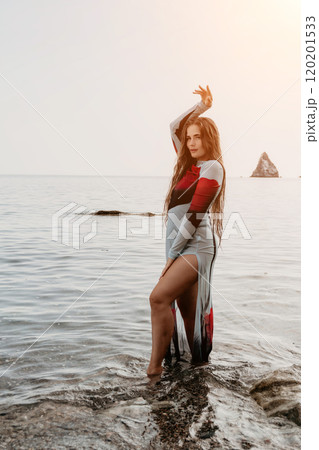 Woman Dress Pose Beach - Fashion model in a colorful dress poses on a rocky beach by the ocean. 120201533