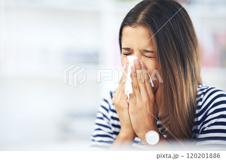 Its allergy season again. Shot of a young woman with allergies sneezing into a tissue at home. 120201886