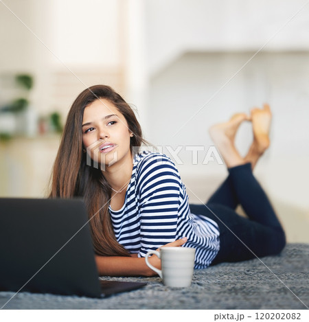 What should I write up next. Shot of a young woman lying on the floor at home using a laptop deep in thought. 120202082