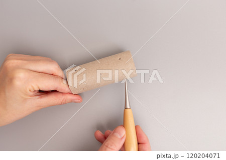part of a creative process involving modifying or repurposing empty toilet paper roll cardboard tube, for a craft or DIY project. using a awl tool with a wooden handle and a metal point , 120204071