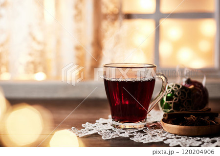 板のテーブルの上にホットワイン、窓辺に写り込むクリスマスライト 120204906