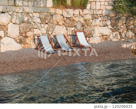 Three empty beach chairs resting by the calm seaside, inviting a peaceful moment by the shore. Three empty beach chairs resting by the calm seaside, inviting a peaceful moment by the shore. 120206835