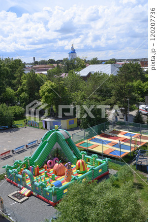 Park with a carousel, trampoline, slides, children and dome of church in summer Park with a carousel, trampoline, slides, children and dome of church in summer 120207736