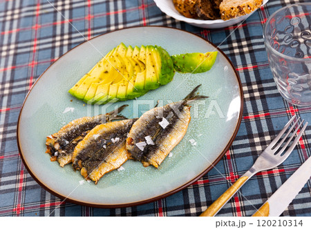 Smoked fillet of sardine carcass is served in plate with slices of ripe avocado. 120210314