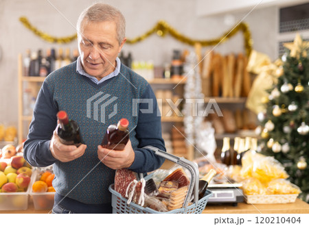 Mature female customer choosing whiskey for Christmas celebration at supermarket 120210404