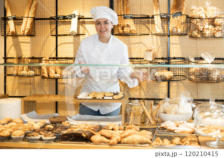 Female baker in a white coat and chef hat invites you to buy fresh bread and buns Female baker in a white coat and chef hat invites you to buy fresh bread and buns 120210415