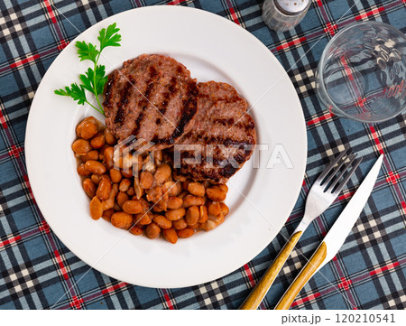 Plate contains light side dish of stewed vegetables - red kidney beans with meat patty 120210541