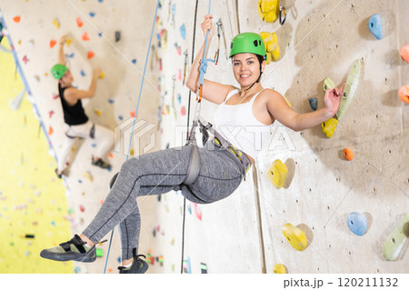 Sporty young girl in safety gear doing difficult wall climb in climbing gym 120211132