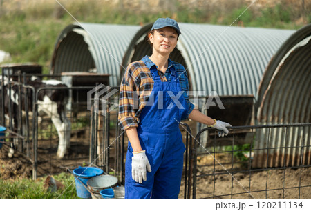 Portrait of female farmerwith bucket against the background of calf pen on summer day 120211134