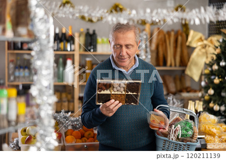 Man prepares to celebrate Christmas by choosing sweet dried fruits in produce section of supermarket 120211139