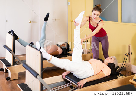 Elderly woman practicing pilates on reformer with young female trainer Elderly woman practicing pilates on reformer with young female trainer 120211697