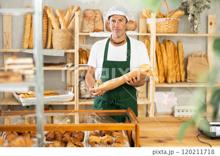Middle-aged salesman holding paper bag with baguettes in bakery Middle-aged salesman holding paper bag with baguettes in bakery 120211718