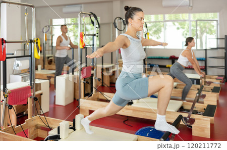 Sportive young girl training her arms and legs on reformer device 120211772