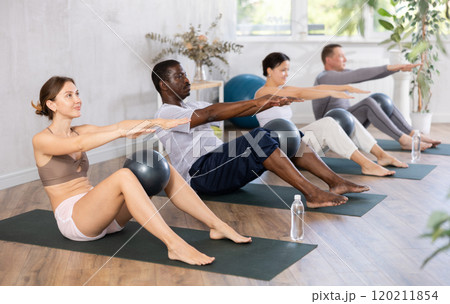 Group of active people doing soft ball pilates exercises during group pilates class in fitness gym 120211854