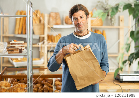 Positive middle-aged guy holding paper bag in bakery 120211989