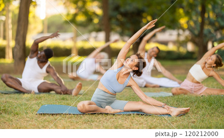 Woman performing Parivrtta Janu Sirsasana during group yoga class in park 120212000