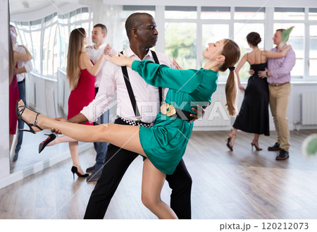 Elegant duet of man and woman in festive dresses dances passionate tango during group dance lesson in choreographic studio Elegant duet of man and woman in festive dresses dances passionate tango during group dance lesson in choreographic studio 120212073