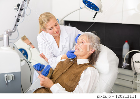 Cosmetologist explaining future facial procedure to elderly female patient Cosmetologist explaining future facial procedure to elderly female patient 120212111