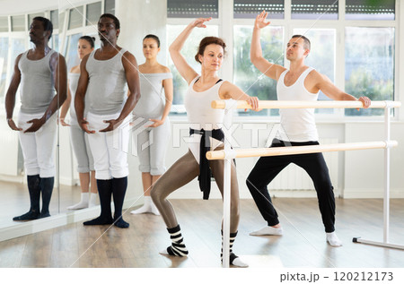 Woman and man dancers practice plie at barre 120212173